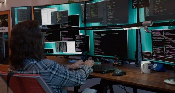 Developer working at a desk surrounded by monitors showing code