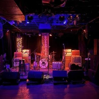 Purple-lit underground venue stage with speakers and arcade-style equipment