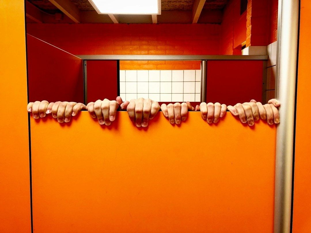 Multiple hands grip the top edge of an orange partition