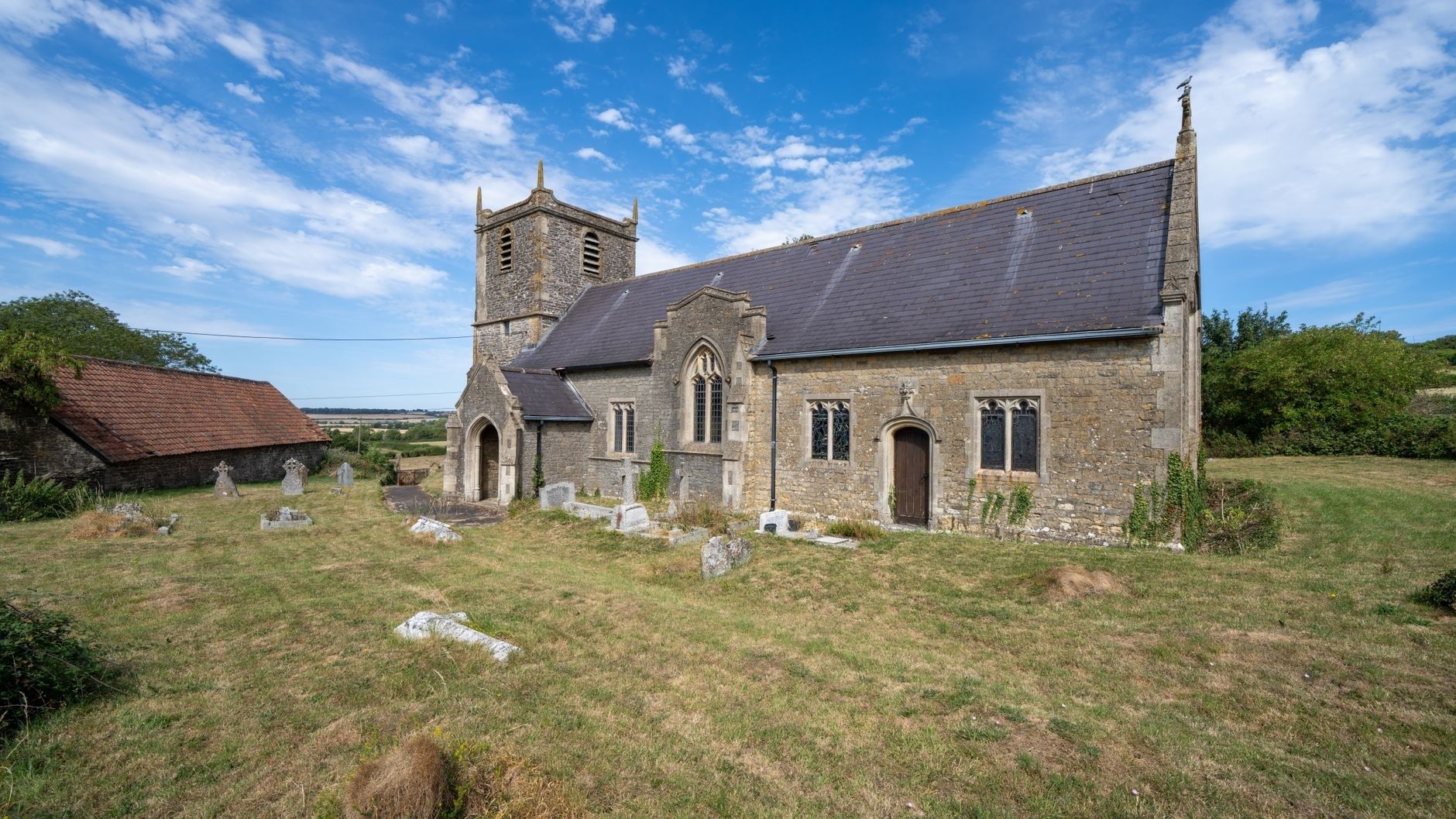 Stone English church and graveyard beneath a bright rural sky